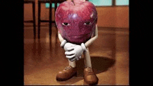 a cartoon apple with arms and legs is sitting on the floor with his hands folded .