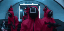 a group of people in red jumpsuits and masks are standing in a tunnel .