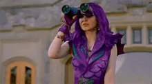 a woman in a purple dress is looking through binoculars in front of a building .