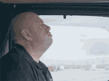 a bald man is sitting in a car with his eyes closed and his mouth open .