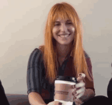 a woman with long red hair is sitting on a couch holding a cup of coffee .