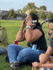 a woman is sitting on the grass talking on her cell phone