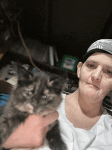 a woman holding a kitten in her arms while wearing a hat