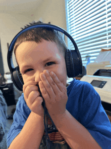 a young boy wearing headphones covering his face with his hands