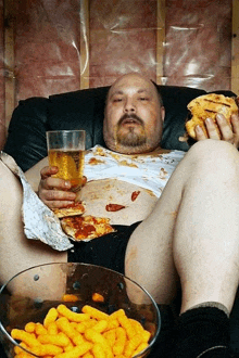 a man is laying on a couch eating cheese puffs and holding a glass of beer