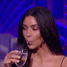 a woman is drinking water through a straw from a glass of water .