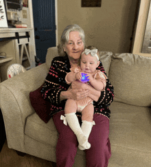 a woman is holding a baby on a couch and the baby is holding a toy