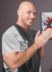 a bald man is clapping his hands in front of a painting of flowers on the wall