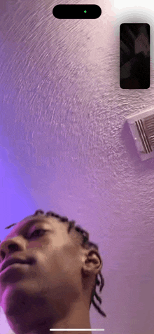 a man with dreadlocks is looking up at a cell phone on a purple wall