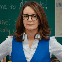 a woman wearing glasses and a blue vest stands in front of a chalkboard that says " me to "