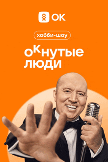 a man in a tuxedo is holding a microphone in front of an orange background that says ok