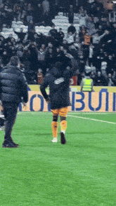 a man in a black jacket stands on a soccer field in front of a sign that says ' bui '