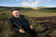 an elderly man is kneeling down in a field holding a stick