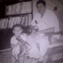 a black and white photo of a man sitting next to a child holding a shoe .