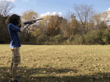 a man with curly hair is holding a rifle in a field