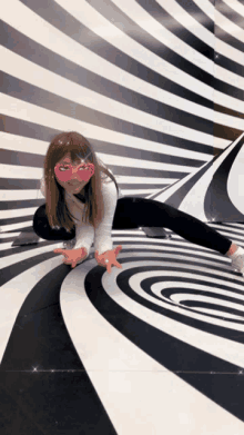 a little girl wearing pink heart shaped glasses is kneeling on a black and white swirl floor