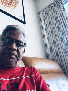 a man sitting on a couch wearing a red shirt with the letter b on it