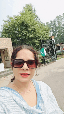 a woman wearing sunglasses takes a selfie in front of a gate with a green and white flag