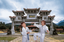 a man and a boy are practicing martial arts in front of a stone archway with chinese writing on it