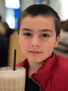 a young boy in a red jacket is holding a milkshake with a straw