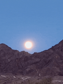 a full moon rises over the mountains in the desert