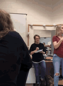 a woman in a red shirt stands in front of a mirror while another woman writes on a piece of paper