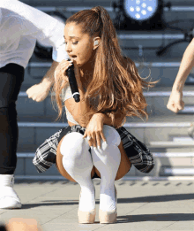 a woman in a plaid skirt and white knee high socks is singing into a microphone on a stage