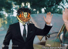 a man in a suit and tie waving in front of a car with panic station pythons on the bottom