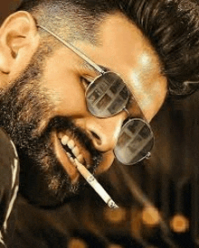 a man with a beard wearing sunglasses and smoking a cigarette .