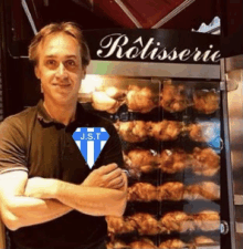 a man in a j.s.t shirt stands in front of a rotisserie oven