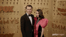 a man in a tuxedo and a woman in a pink dress pose on the red carpet at the emmys