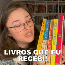 a woman wearing glasses is holding a stack of books with the words " livros que eu recebi " above her