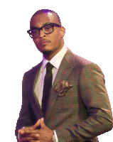 a man wearing glasses and a plaid suit is standing with his hands folded