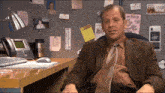 a man in a suit and tie sits at a desk in front of a wall with papers on it including one that says ranger