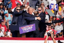 donald trump is being hugged by a group of people at a campaign rally .