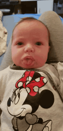 a baby wearing a minnie mouse shirt is sticking out its tongue