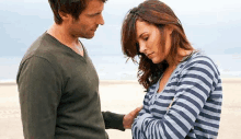 a man and a woman are standing next to each other on the beach . the woman is wearing a striped shirt .