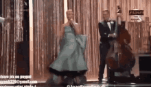 a woman in a green dress is singing into a microphone while a man plays a double bass behind her