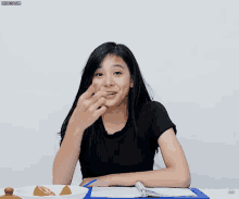 a girl in a black shirt is sitting at a table with a clipboard and a bowl of lemon slices