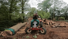 a man sits on a red tractor in a field of logs