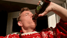 a man in a red and white sweater is drinking from a bottle with a green label that says ' ss '