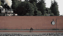 a man sits on a bench in front of a train and a clock which shows the time as 2:30