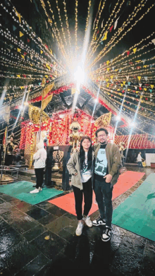 a man and a woman are posing for a picture in front of a building with flags on it