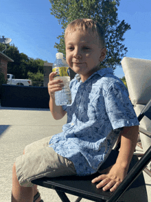 a young boy in a blue shirt is holding a bottle of water with a yellow label