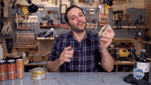 a man in a plaid shirt is standing in front of a workbench with a bottle of mundial mundo on the table