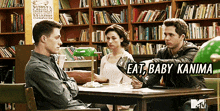 a group of people are sitting at a table in a library with a sign that says eat baby kanima