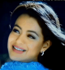 a close up of a woman wearing a blue dress and earrings smiling