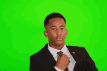 a man in a suit and tie adjusts his tie against a green background