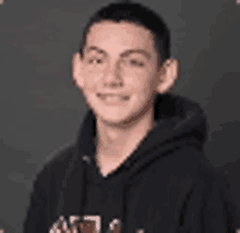 a young man is wearing a black hoodie and smiling .