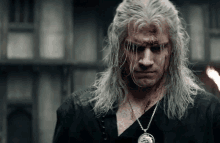 a man with long white hair and a necklace with a coin on it